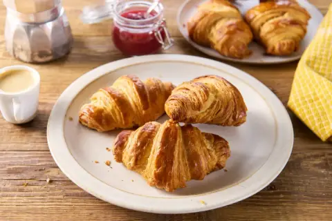 Talerz z trzema złotymi croissantami, filiżanka kawy, słoiczek dżemu i kawiarka.
