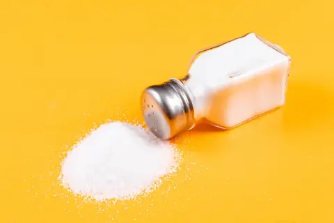 Salero volcado con sal yodada o normal derramada sobre fondo amarillo.