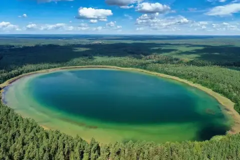 Widok z lotu ptaka na **jezioro płaskie** otoczone lasem. Woda ma turkusowy odcień, a brzegi są porośnięte drzewami.