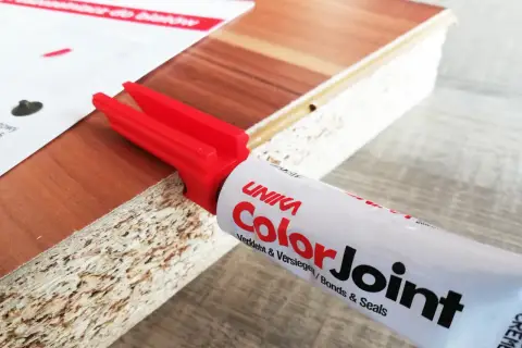 Klej do blatów ColorJoint i czerwony aplikator na krawędzi płyty meblowej.