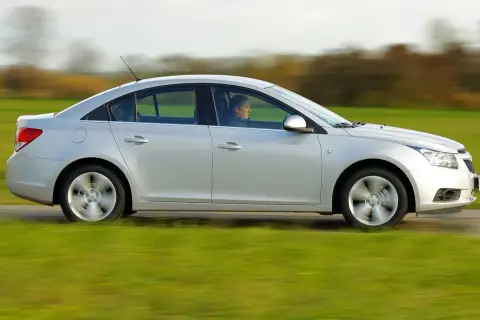 Srebrny Chevrolet Cruze 1.8 benzyna w ruchu, z kierowcą za kierownicą, przemierza wiejską drogę pośród zielonych pól.
