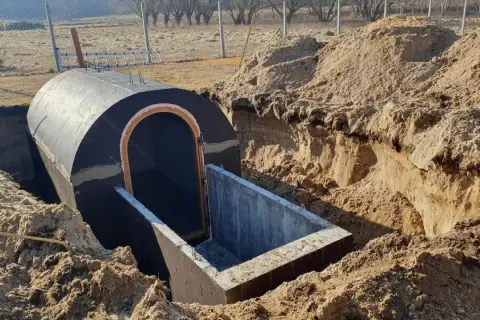 Budowa piwnicy ziemianki w trakcie. Okrągły, betonowy tunel z wejściem wkopany w ziemię, otoczony usypanym piaskiem.