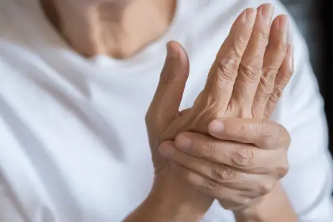Dłoń uciskana przez drugą, ukazująca bóle reumatyczne rąk.