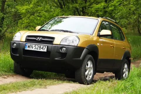Złoty Hyundai Tucson 2007 na leśnej drodze, gotowy na przygodę.