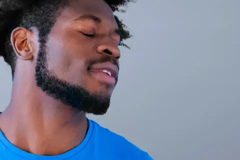Hombre con ojos cerrados y barba cuidada, parece disfrutar de un momento de paz. Sus perillas resaltan su rostro.