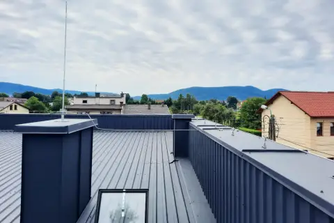 Nowoczesna instalacja odgromowa na dachu z blachy, chroniąca budynek przed burzą. Widok na góry w tle.