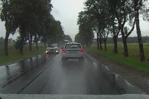 Deszczowa droga, samochód z przodu ma włączone światła mijania, a nasz samochód z tyłu jedzie na światłach dziennych.