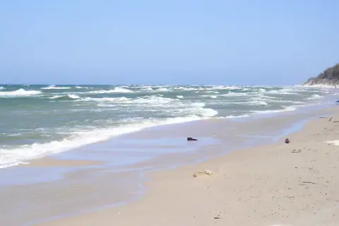Plaża w Rowach, z falującym morzem i piaszczystym brzegiem. W oddali widać wydmy i nielicznych spacerowiczów.