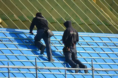 Dwaj dekarze układają membranę dachową, kluczowy element ochrony domu przed wilgocią.