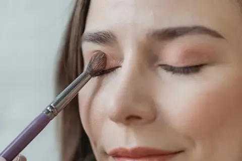 Eine Frau trägt mit einem Pinsel sanft Lidschatten auf. So gelingt das lidschatten richtig auftragen für einen strahlenden Blick.