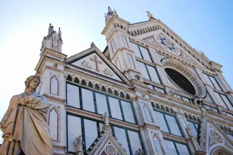 Statua di un poeta toscano davanti alla facciata in marmo di una chiesa fiorentina.