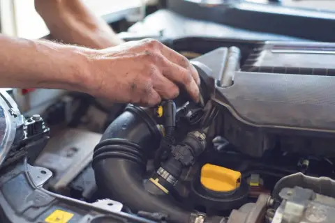 Ręce mechanika pracujące przy silniku samochodu, widoczne przewody i żółta zakrętka.