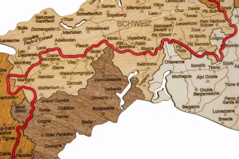 Drewniana mapa Alp z zaznaczoną trasą Via Alpina, pokazująca szczyty i miejscowości takie jak Matterhorn, Zermatt, Lugano i St. Moritz.