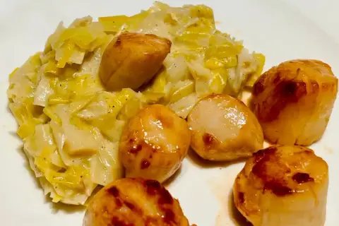 Saint-Jacques poêlées sur un lit de fondue de poireaux crémeuse, un plat savoureux et réconfortant.