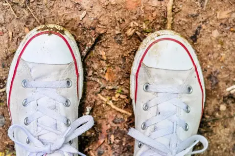 Białe trampki z czerwonymi akcentami, lekko zabrudzone ziemią, czekają na czyszczenie.