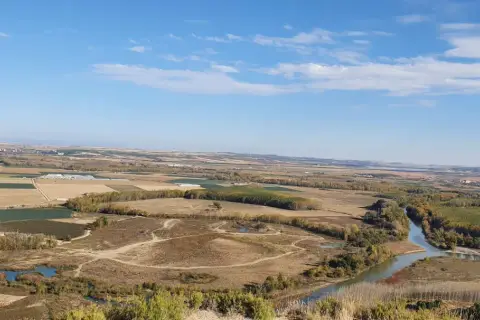 Paisaje rural con un río serpenteante cerca de Villafranca del Bierzo. Campos cultivados y árboles de otoño bajo un cielo azul con nubes.