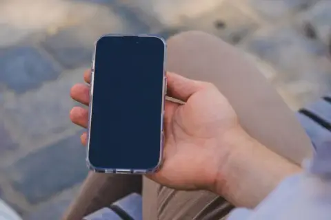 Mężczyzna trzyma iPhone'a w przezroczystym etui. Zastanawia się, jak wyłączyć iPhone'a, aby oszczędzić baterię.