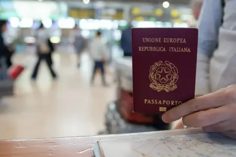 W podróży do Irlandii, czy do Irlandii potrzebny jest paszport? W ręku włoski paszport, na tle lotniska.