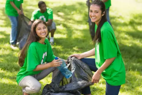 Students participate in community service projects, cleaning up a park and smiling as they collect trash.