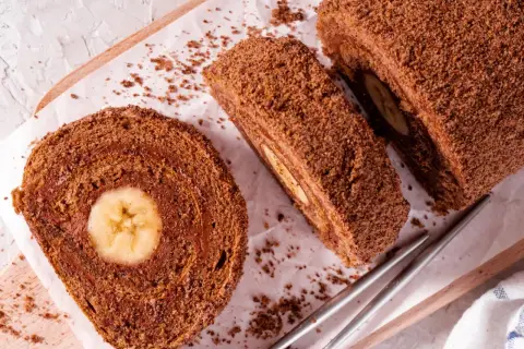 Czekoladowa, najprostsza rolada biszkoptowa z bananem w środku, posypana kakao. Idealna na deser.