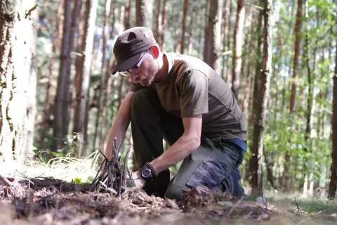 Mężczyzna w lesie przygotowuje rozpałkę. To pokazuje, survival co to znaczy: umiejętność radzenia sobie w trudnych warunkach.
