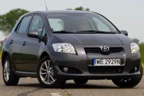 Szary Toyota Auris 2015 na drodze, z zielonym polem w tle.