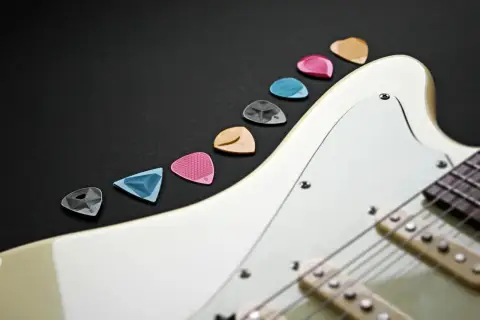 Kolorowe kostki do gitary elektrycznej leżą obok białej gitary. Zastanawiasz się, jak nastroić gitarę elektryczną? Zacznij od wyboru odpowiedniej kostki!
