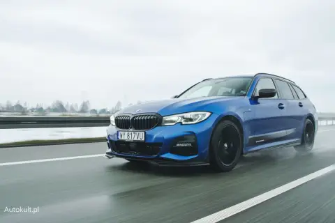 Niebieskie BMW 330e na mokrej drodze, z widocznymi kroplami deszczu na karoserii.