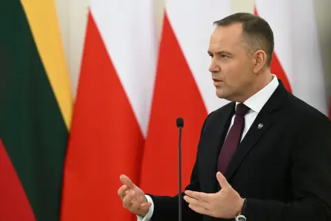 Karol Nawrocki, w garniturze, przemawia na tle flag. Jego gestykulacja i pewność siebie mogą być powodem, dlaczego Karol Nawrocki stał się nowym liderem sondaży zaufania na prawicy.