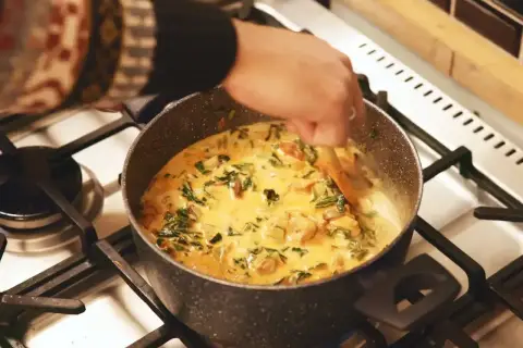 Ręka miesza kremowe curry z zielonymi warzywami w garnku. Idealny garam masala przepis na aromatyczne danie.