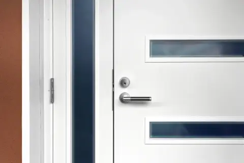 Nowoczesne białe drzwi wejściowe z metalową klamką i wąskimi, ciemnymi przeszkleniami. Dowiedz się, jak zmierzyć drzwi wejściowe.
