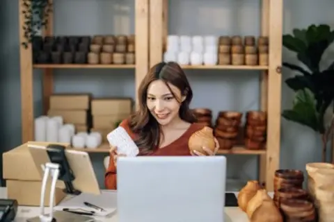 Kobieta prezentuje produkty do swojego sklepu na Facebooku, trzymając w rękach drewniane przedmioty.