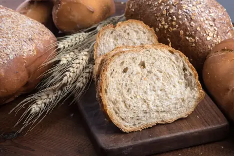 Różnorodne pieczywo, w tym bochenki z ziarnami i kromki chleba pełnoziarnistego. Idealne, gdy zastanawiasz się, jakie pieczywo przy odchudzaniu wybrać.