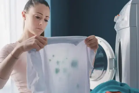 Kobieta z niedowierzaniem patrzy na poplamioną koszulkę, która wyszła z pralki.