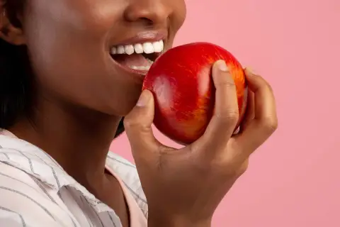 Une femme souriante tient une pomme rouge, un coupe faim naturel parfait pour une pause saine.