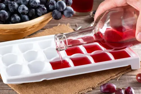Czy warto mrozić wino do późniejszego wykorzystania w kuchni? Czerwone wino wlewane do pojemnika na lód, obok kiści winogron.