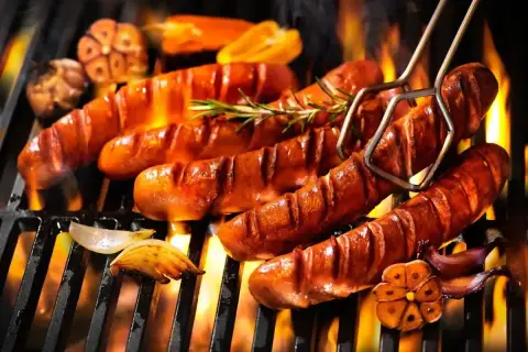 Aromatyczna kiełbasa z grilla skwierczy na ruszcie, otoczona płomieniami i przypieczonym czosnkiem.