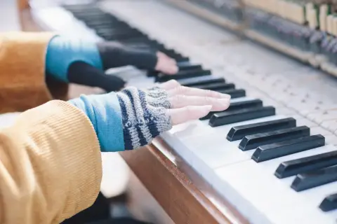 Les doigts de pianiste, vêtus de mitaines colorées, effleurent les touches d'un piano, créant une mélodie douce.