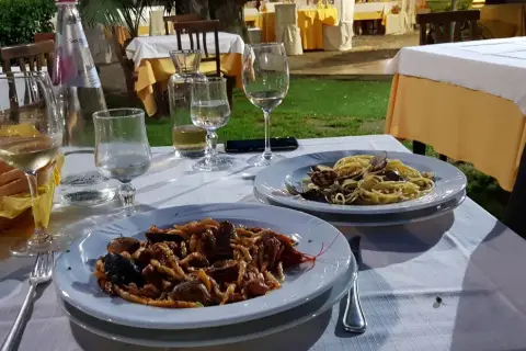 Dwa talerze z makaronem i owocami morza, kieliszki z winem i woda na stole w restauracji pod gołym niebem.