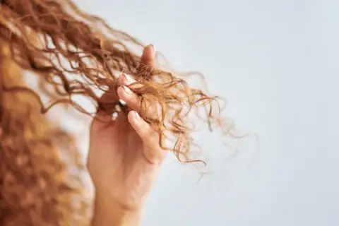 Mano acariciando cabello rizado, mostrando cómo rizar el pelo con espuma para definir ondas.
