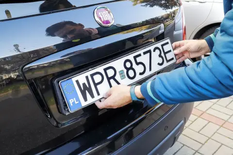 Ręce montują tablicę rejestracyjną. Uniknięcie mandatu za brak tablicy rejestracyjnej jest ważne.