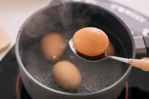 Une cuillère sort un œuf à la coque de l'eau bouillante. Trois autres œufs sont dans la casserole.