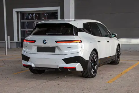 Białe BMW iX z czarnymi akcentami stoi na parkingu.