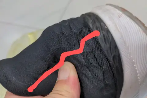 Un pouce appuie sur le contrefort d'une chaussure noire, révélant une fissure.