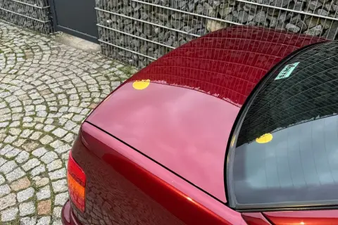 Błyszczący, czerwony lakier włoskiego auta sportowego odbija kamienną kostkę i gabionową ścianę.