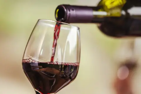 Czerwone wino nalewane do kieliszka. Widoczne "łzy" na ściance, świadczące o zawartości alkoholu.