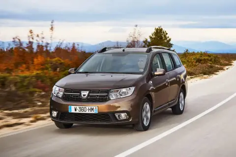 Brązowy Dacia Logan MCV jedzie po krętej drodze wśród jesiennych drzew i gór w tle.