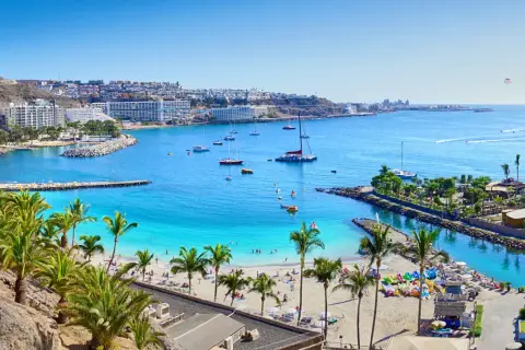 Gran Canaria loty bezpośrednie: słoneczna plaża, palmy, turkusowa woda i białe budynki hotelowe tworzą rajski widok.