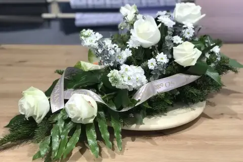 Białe róże na drewnianym stole, ozdobione wstęgą. Biała róża symbolizuje czystość i niewinność, często wybierana na uroczystości.