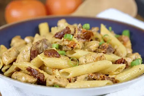 Penne z kurczakiem i suszonymi pomidorami, posypane szczypiorkiem. Pyszne danie, które zachwyci każdego smakosza.